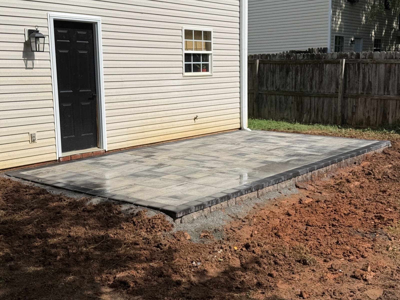 A side-by-side comparison of a paver patio and stamped concrete patio in a backyard setting.